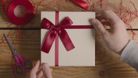 Fotografía-Cenital-Del-Hombre-Que-Envuelve-Un-Regalo-Romántico-Regalo-De-San-Valentín-De-Perfume-En-Una-Caja-En-La-Mesa-1