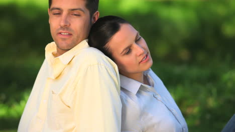 lovers sitting back-to-back on the grass