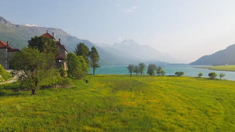 serene lake surrounded by mountains, cottage, and lush meadow in a tranquil setting. aerial, push forward