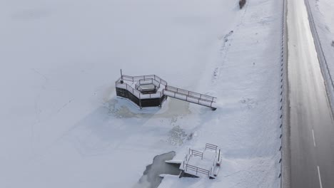 drone captures a snowy road with a frozen lake and dam structure in a serene baltic setting