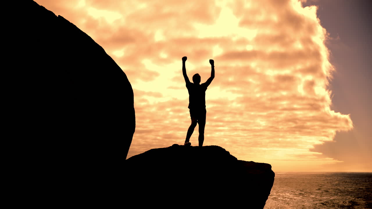 Silhouette of a person celebrating success on a cliff at sunset