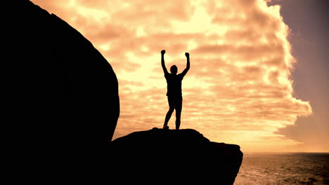 silhouette of a person celebrating success on a cliff at sunset