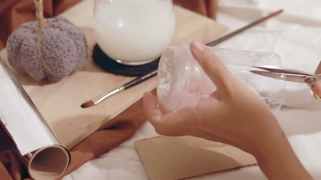 Cutting plastic bottle for a creative DIY recycling craft project on a table with a cozy autumnal setup