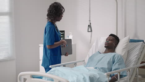 a black female doctor is talking to a black male patient lying on a hospital bed and connected to an acid supply