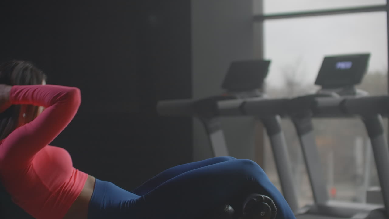 젊은 여성은 체육관에서 복부 운동을 하고 있습니다. 그녀는 그녀의 호흡과 기법을 통제하고 있습니다. 그녀는 매번 쪽을 바꾸고 있습니다. 이것은 피트니스 센터에서 생산적인 아침 운동입니다.