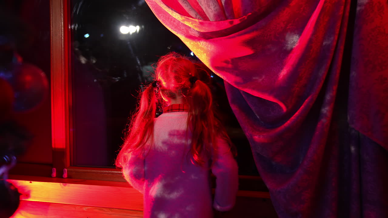 Little girl waiting for Santa Claus. Girl looks out the window during winter evening near the Christmas tree