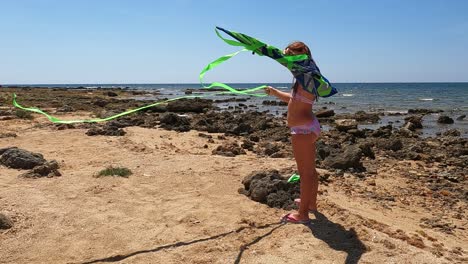 cute little girl on summer holiday in swimsuit on the beach prepares to play with a green toy kite