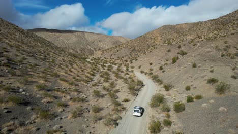 view above white car off roading in desert hills, aerial view