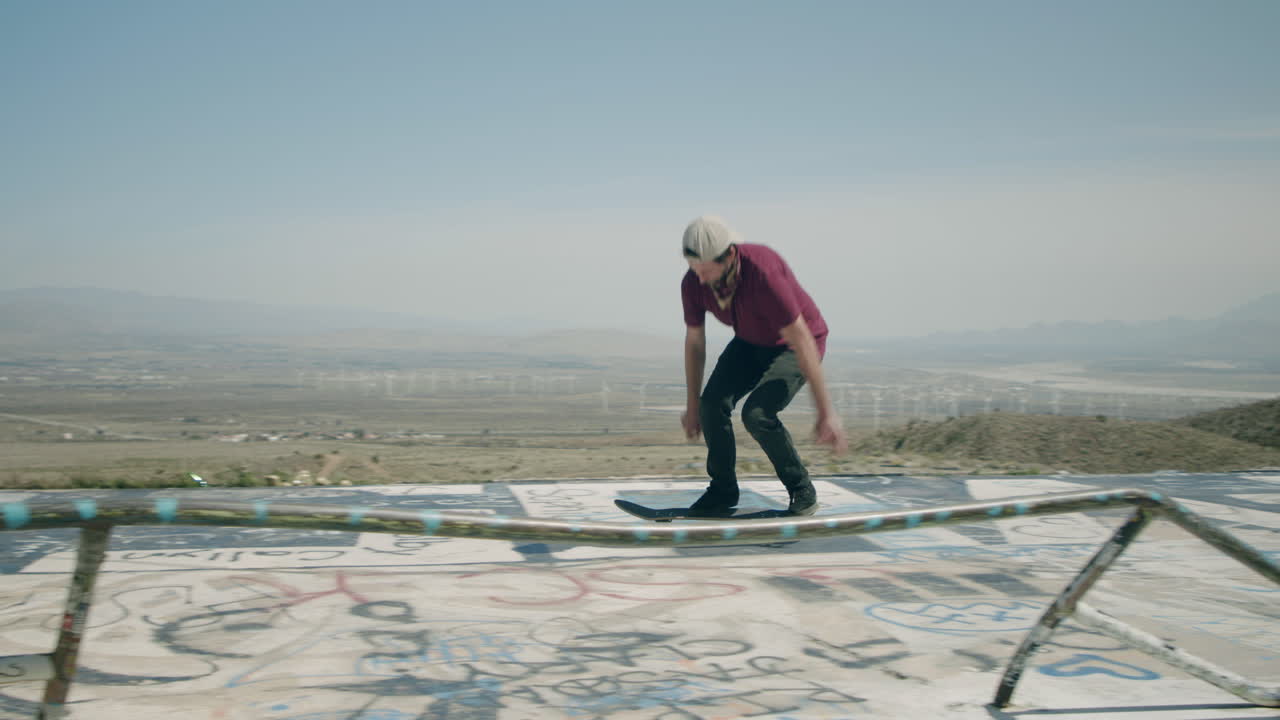 Skateboarder performing tricks on a graffiti-covered surface with a wind farm in the background