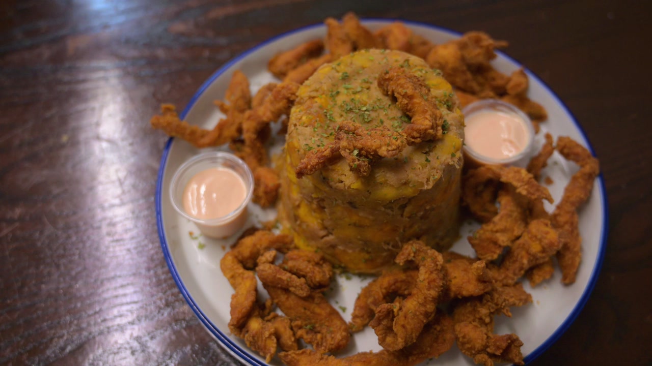 Cinematic high angle shot of a traditional Puerto Rican mofongo. Mashed green plantains served with fried meat and side sauces in a restaurant setting.