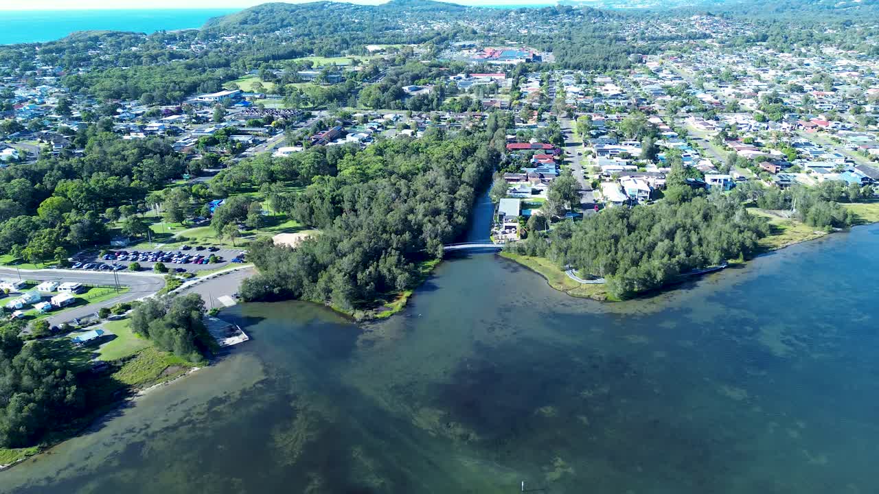 Drone aerial landscape of pathway bridge over lake creek water inlet surrounded by rural town housing, trees and public carpark Long Jetty Killarney Vale Central Coast Australia travel tourism nature