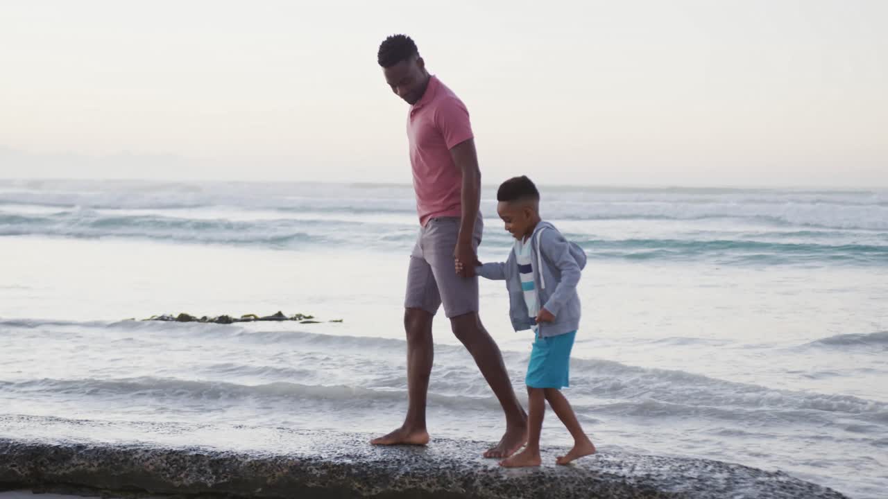 African american father walking with son on sunny beach