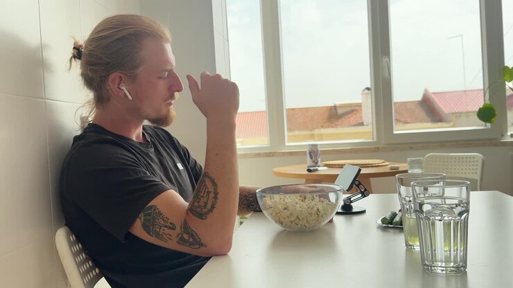Giovane uomo che mangia popcorn e guarda contenuti sullo smartphone a casa.