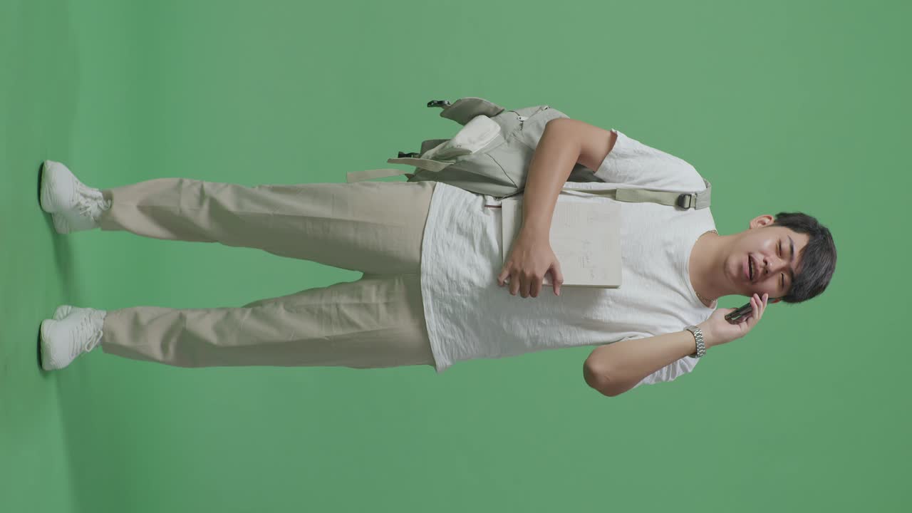 녹색 스크린 스튜디오에서 휴대전화로 대화하는 아시아 남성 학생의 몸이 가득 차 있습니다.