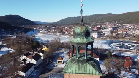 wunderschöne winterliche luftaufnahme der stadt kongsberg mit der spitze des kirchturms im vordergrund - luftaufnahme, die langsam um den kirchturm kreist und dabei an einem sonnigen wintertag den vollen panoramablick auf die stadt freigibt