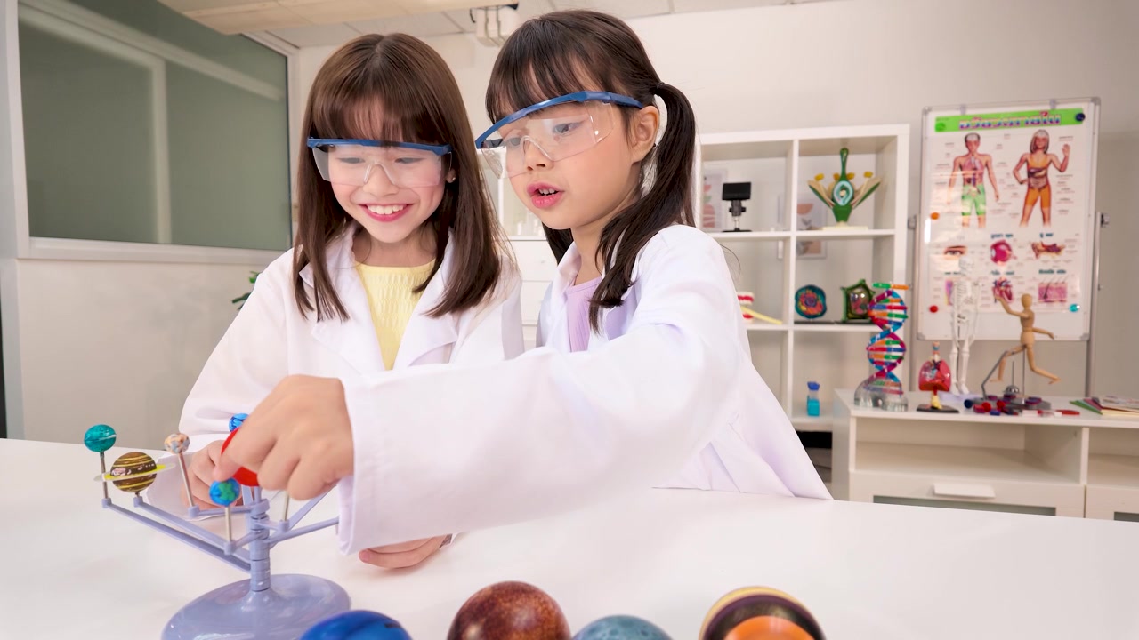 Two Young Girls in Lab Coats Studying Solar System Model