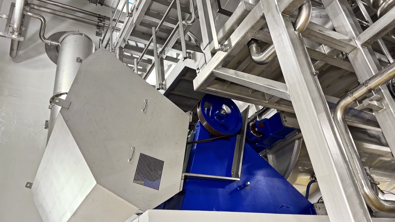Blue industrial motor beneath steel framework in processing plant interior, wide overview, pulsing and bouncing