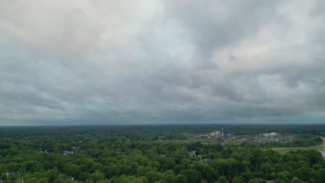 Eine-Dramatische-Luftaufnahme-Eines-Bewölkten-Himmels-über-Einer-üppig-Grünen-Landschaft-Mit-Einem-Industriegebiet-In-Der-Ferne