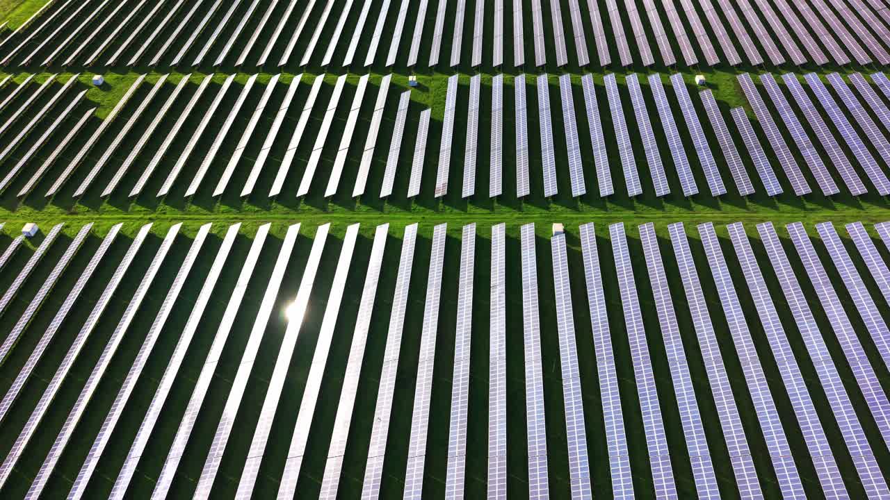 Solar panels arranged in orderly rows on green field from above