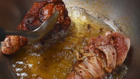 two chicken drumsticks frying in a pan being turned on the other side revealing golden brown meat making an inviting meal