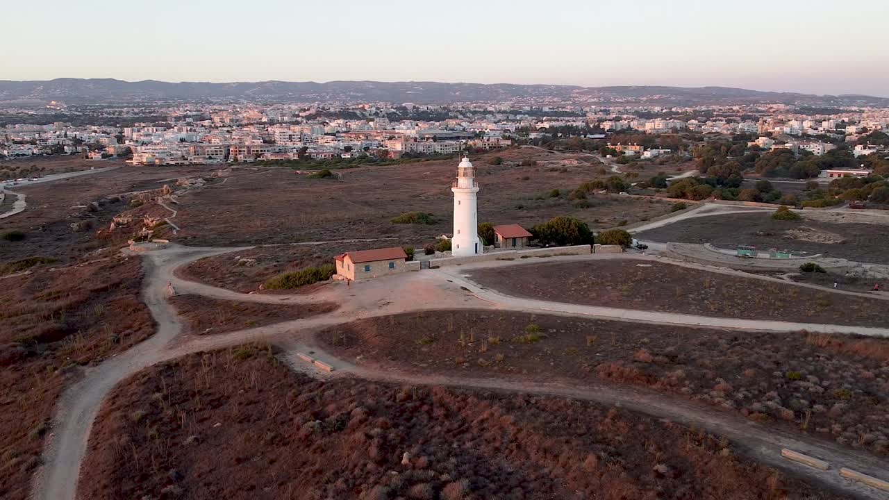 Witness the beauty of a lighthouse surrounded by a serene landscape at sunset in Cyprus. This scene showcases the coastal charm and nature of the area, perfect for outdoor lovers