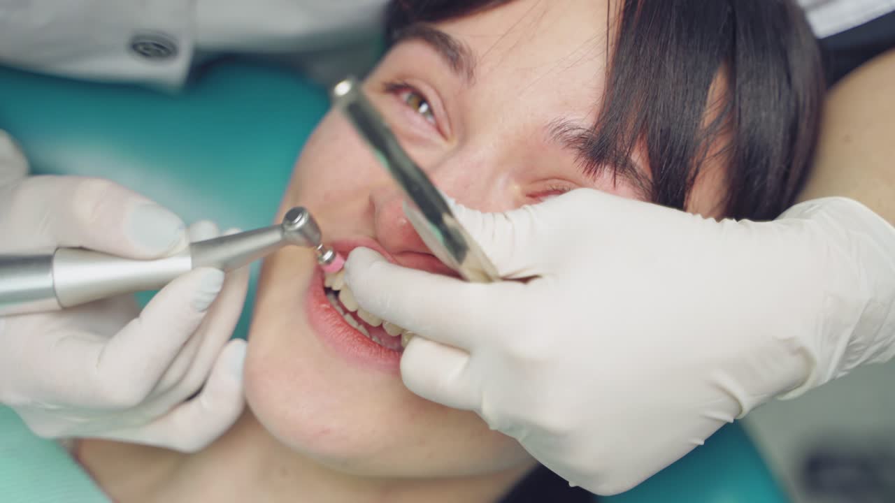 Dental hygienist polishing patient teeth in cosmetic dentistry clinic. Close up of a specialist working with patient in dentist office. Female patient moans a little during her visit at dentist.