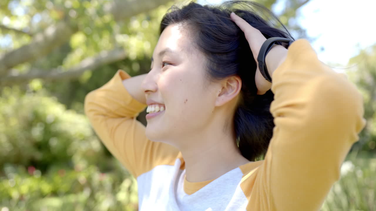 Holding head with hands, smiling asian woman outdoors enjoying nature