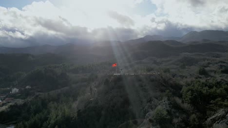 fluttering flag of montenegro with sky rays penetrating dark clouds, dramatic aerial panorama