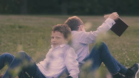 boys-wearing-shirts-and-jeans-lean-backs-sitting-on-lawn