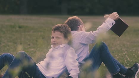 boys wearing shirts and jeans lean backs sitting on lawn