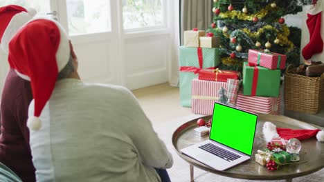 Senior-caucasian-couple-in-santa-hats-making-laptop-christmas-video-call,-with-green-screen