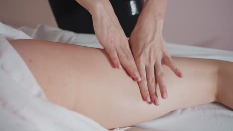 massage therapist pressing down on client thigh using four fingers with focused technique, client lying under white sheet in relaxing room with soft lighting and calming ambiance