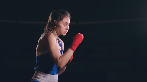 a beautiful woman conducts a shadow fight while practicing hard for future victories. dark gym background. steadicam shot