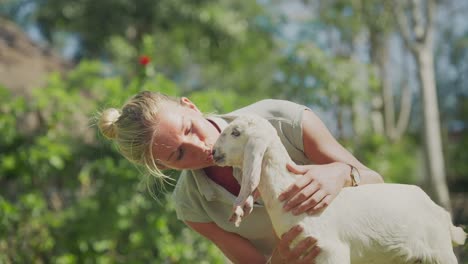 Happy-woman-cuddling-and-kissing-adorable-baby-Nubian-goat,-petting-zoo