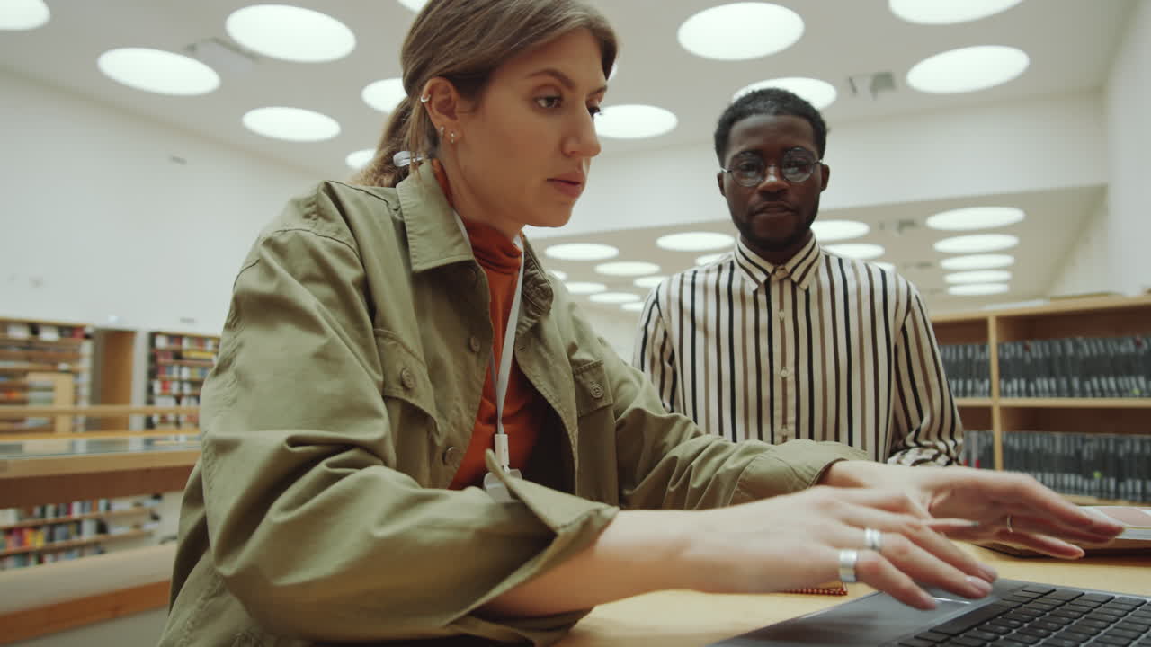 Female Library Worker Using Laptop and Speaking with Afro Man