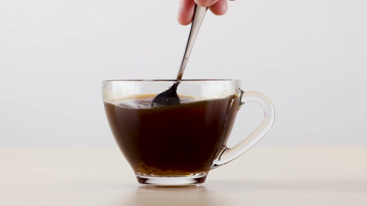 Mano revuelve café negro con cuchara en una taza de vidrio sobre fondo de estudio blanco