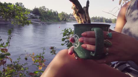 cute hipster girl relaxing by a river or lake with a mug