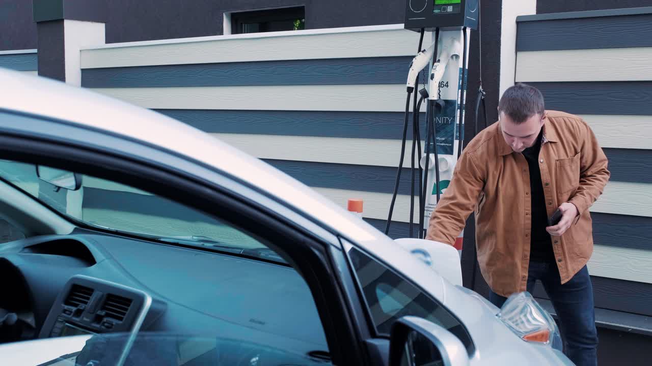 전기 자동차의 연료 충전 과정: 전기 에코 자동차가 충전하는 치 아래의. 전기 자동차 충전 치는 자동으로 열립니다. 남성 손이 발기 된 자동차를 입합니다.