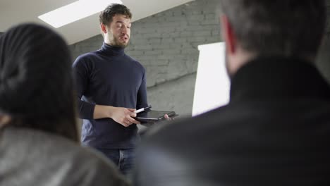 Hübscher-Junger-Geschäftsmann,-Der-Während-Der-Präsentation-Im-Konferenzraum-Auf-Flipchart-Zeigt-Und-Ein-Tablet-In-Der-Hand-Hält.-Präsentationsrede-Mit-Flipchart-Im-Büro.-In-4k-Gedreht