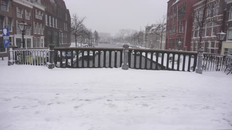 Leiden-in-winter-snow,-tilt-up-shot-on-bridge-over-river-Rijn-Rhine,-Netherlands