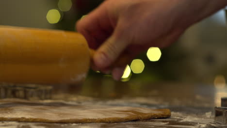 manos masculinas usando un rodillo para aplanar la masa de pan de jengibre en la cocina