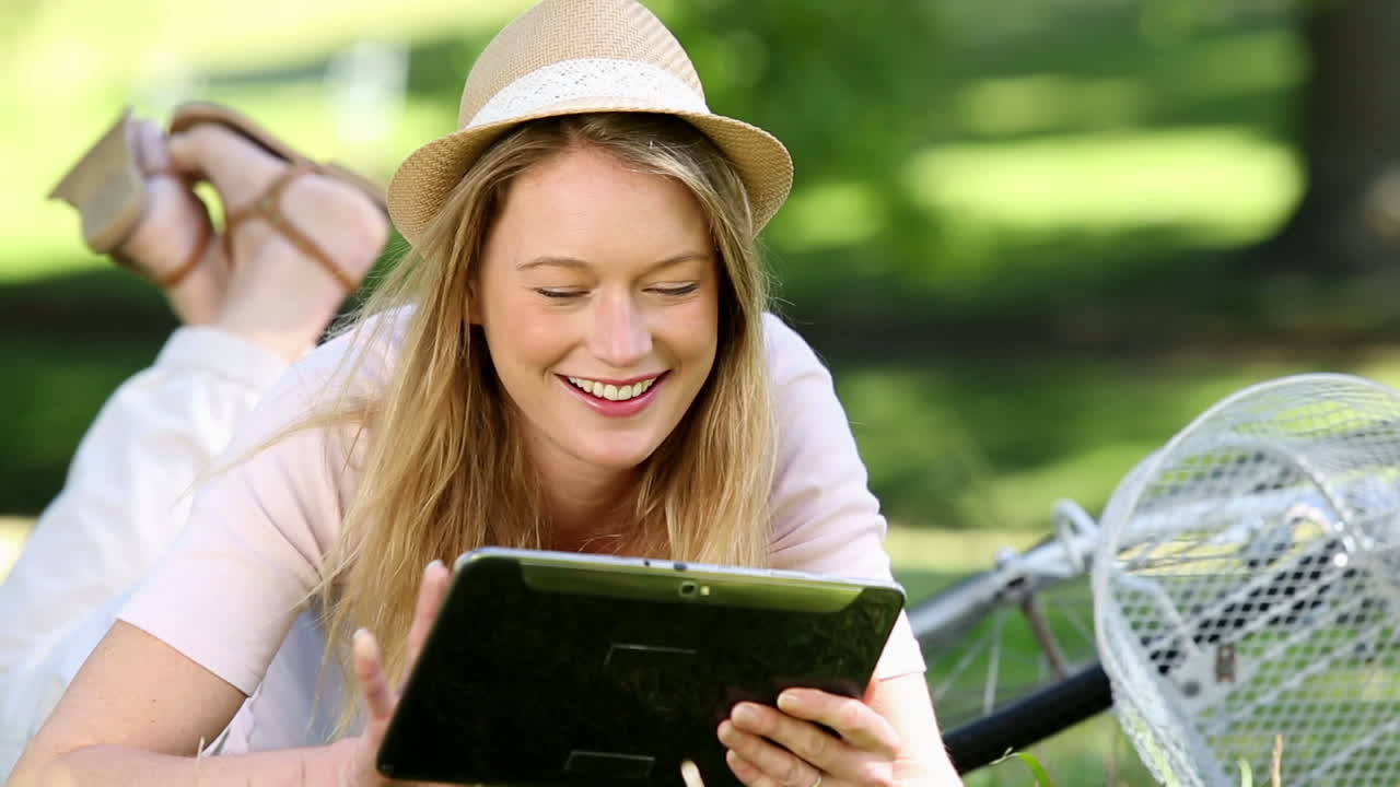 Smuk pige bruger en tablet-pc ved siden af sin cykel i parken