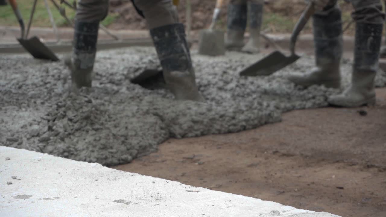 With their boots on wet concrete, workers with shovels pave a street