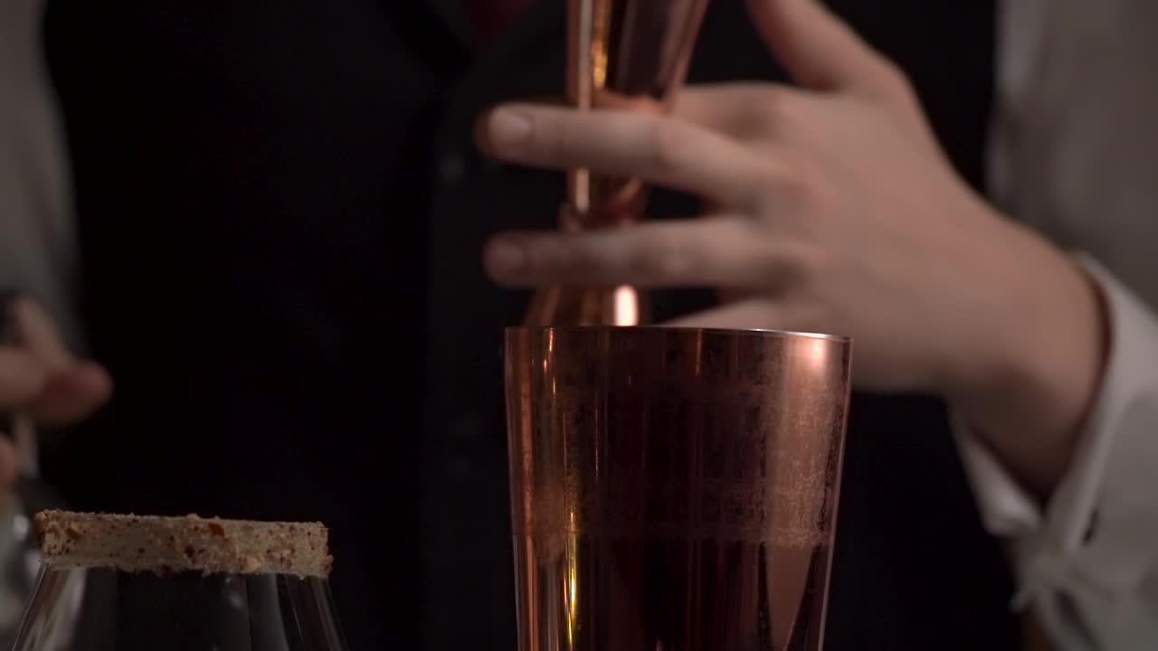 A bartender is pouring spirit into the jigger then to the copper-tin.