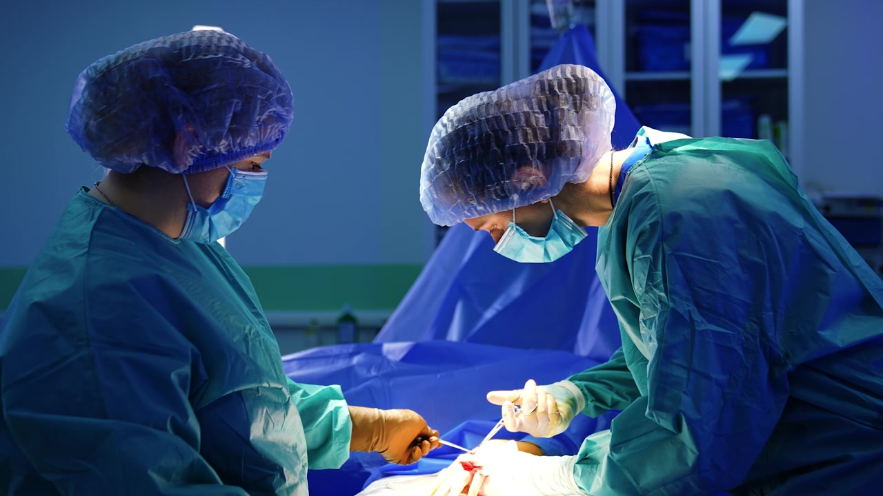 Kvindelig læge og operationssygeplejerske udfører operation. Sygeplejersken holder instrumentet, mens kirurgen anvender metaltang.
