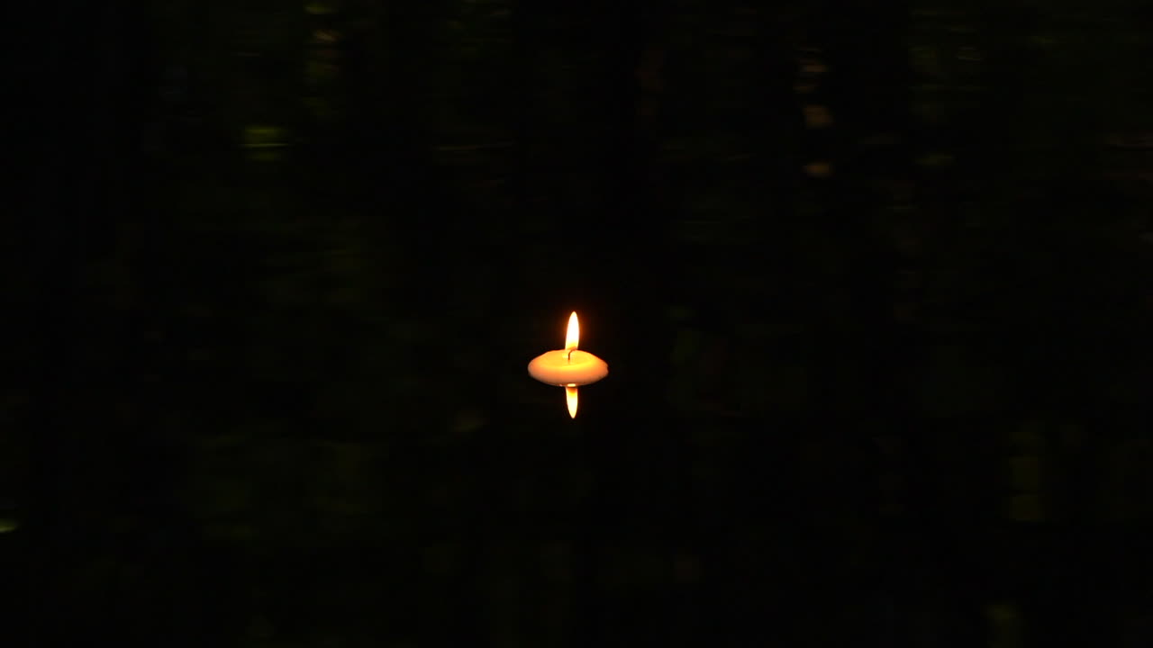 Candela galleggiante in una pozza d'acqua scura con riflesso.