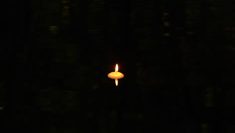 floating candle in dark pool of water with reflection