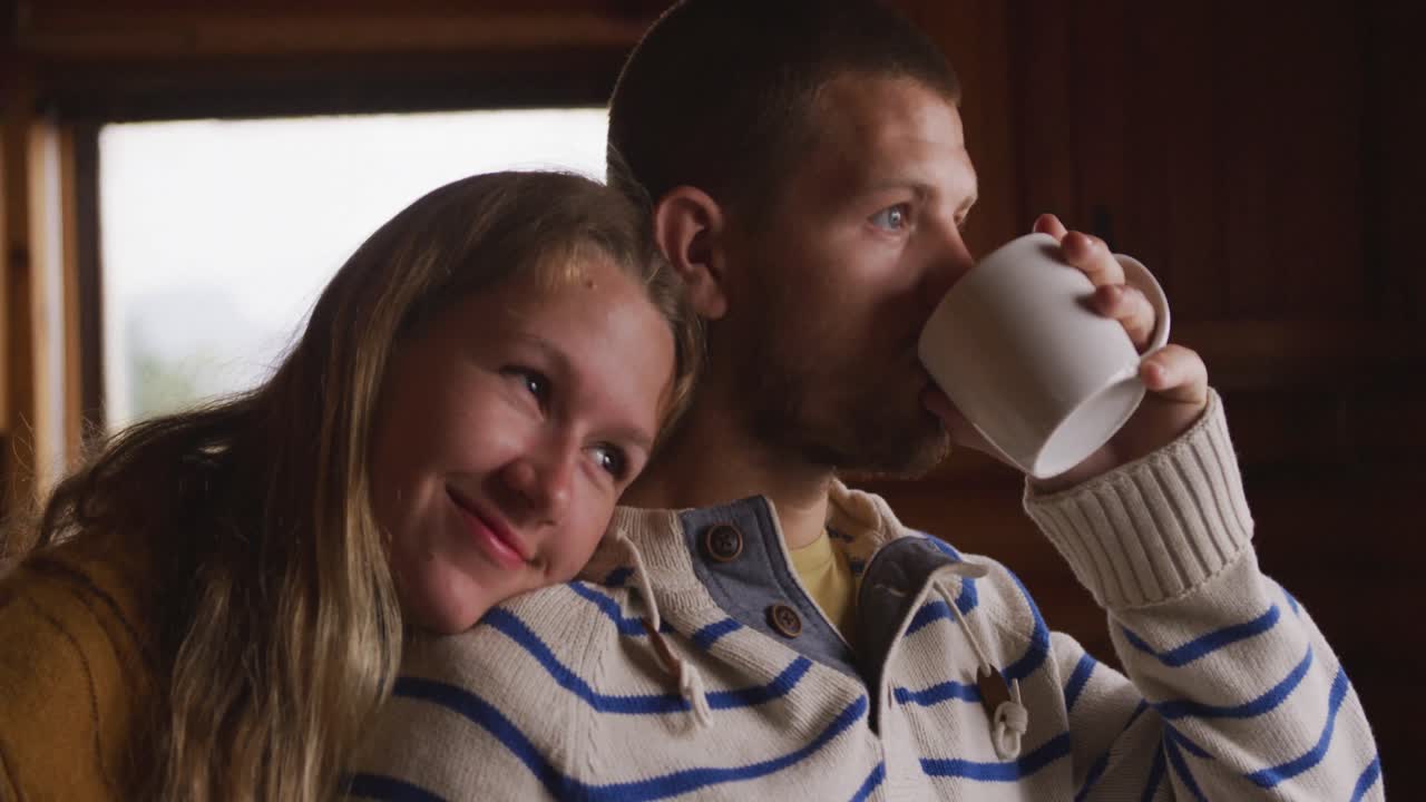 백인 부부가 집에서 함께 시간을 보내고 창문을 쳐다보고 음료를 마시고 있습니다.