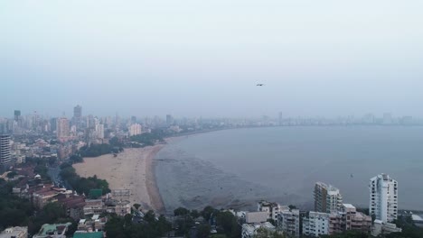 una toma cinematográfica de un dron del famoso punto de playa chaupati de marine drive en la región sur de bombay de la ciudad de mumbai, con vistas a la colina del jardín colgante y al bosque en cámara lenta y suave