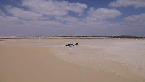 los coches se estacionan en la arena bajo un cielo nublado en el desierto - cámara fija